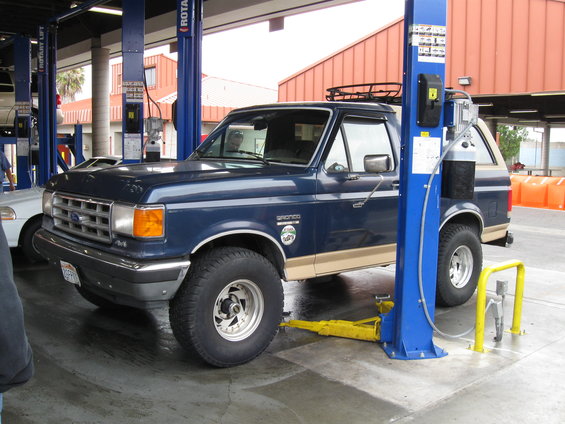 Blue Ford Bronco with tan lower trim and roof rack, parked on a car lift