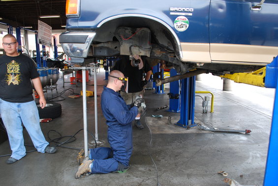 Blue 1986 Ford Bronco on a lift, side view, with mechanics working underneath