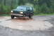 1995 Ford Bronco - A black SUV navigates a large muddy puddle, kicking up water and dirt.