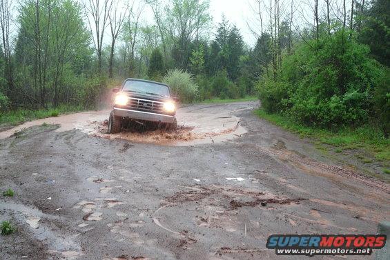 Ford Bronco driving through a muddy puddle on a dirt road