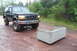 1995 Ford Bronco - A black 1995 Ford Bronco with off-road tires sits on a muddy track next to a concrete structure.