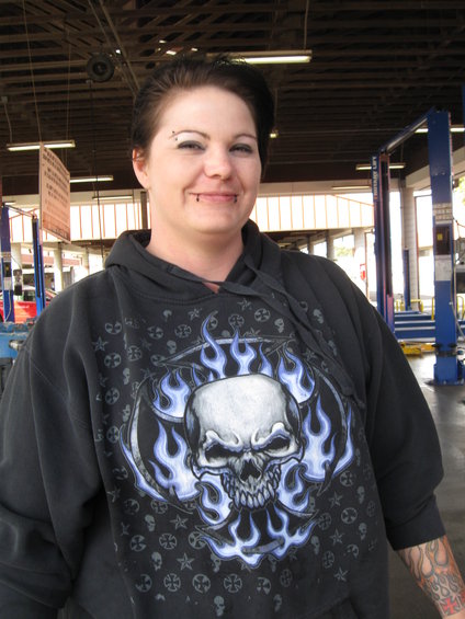 Woman in a skull-themed hoodie smiles in a garage with car lifts in the background