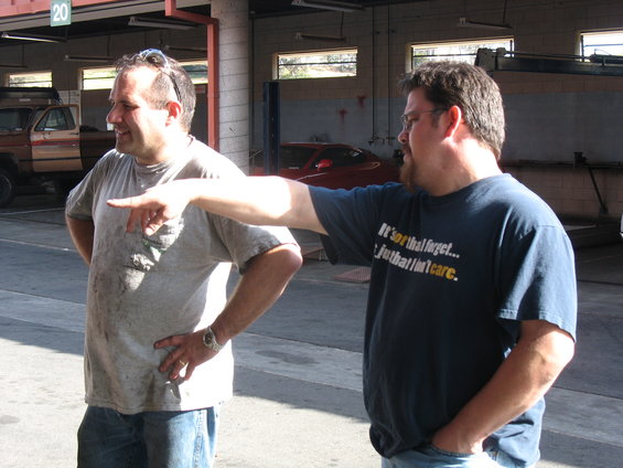 Two men in a garage, one pointing