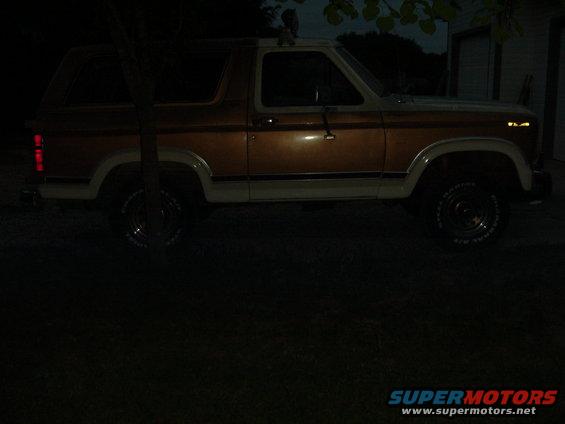 Brown and white Ford Bronco parked at night, side view