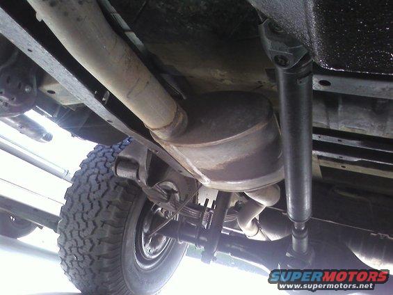 Underside view of a vehicle showing the exhaust system, driveshaft, and rear tire
