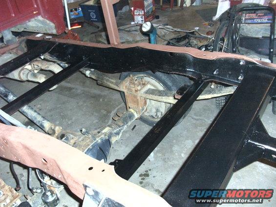 Red truck frame and rear axle assembly with leaf springs, undergoing restoration