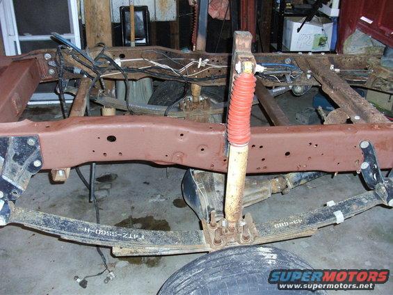 Close-up of a truck's frame and rear suspension with a red-booted shock absorber. Leaf springs are visible, one with part number F4TZ-5560-H