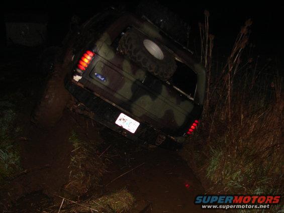 1996 Ford Bronco with camouflage paint stuck in mud at night, rear view