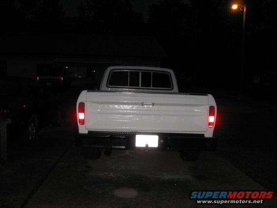 White pickup truck rear view at night. Black bumper, rectangular taillights, and a license plate area are visible