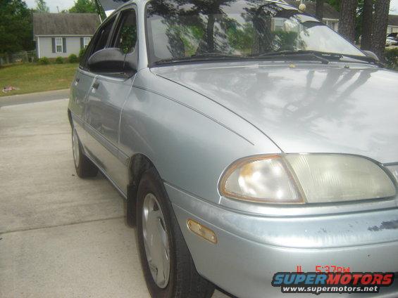 Silver sedan parked on a driveway. Trunk is open. Houses and trees in background