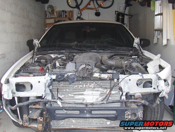 White 2003 Ford Crown Victoria with front end damage, hood open, engine exposed, in a garage