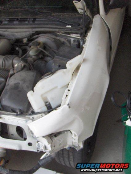Damaged white car fender and engine compartment. The fender is crumpled