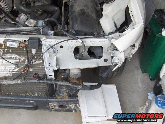 Damaged front end of a white 2003 Ford Crown Victoria, showing the grille and engine components