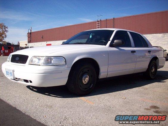 White 2003 Ford Crown Victoria sedan parked on asphalt, front quarter view. Black grille and steel wheels