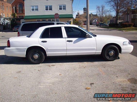 White sedan parked on asphalt, side view. Buildings and a stop sign in background
