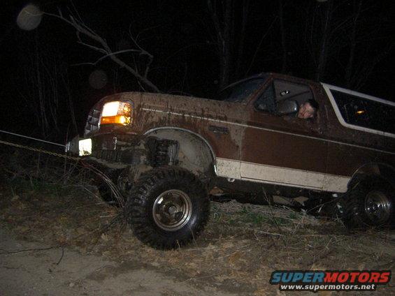Mud-covered 1992 Ford Bronco with headlights on, pulled by a chain