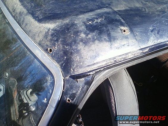 Close-up of a dark blue car roof showing rust damage and several drilled holes near the windshield frame