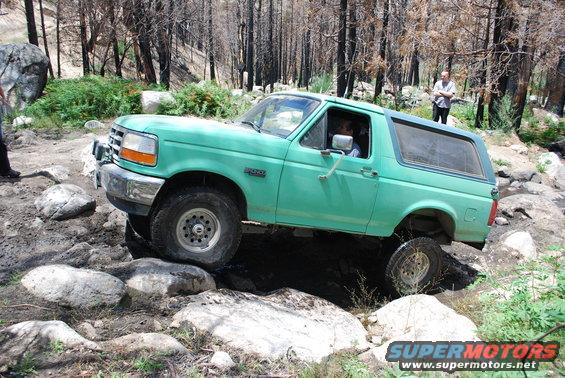 Green Ford Bronco navigating rocky terrain with trees in background