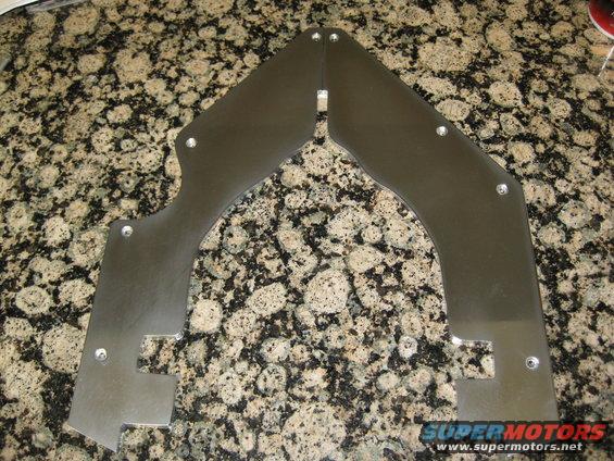Two polished metal plates with cutouts and screw holes on a speckled countertop