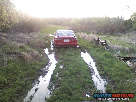 Red 1997 Subaru Legacy sedan stuck in a muddy, grassy path with the rear facing the camera