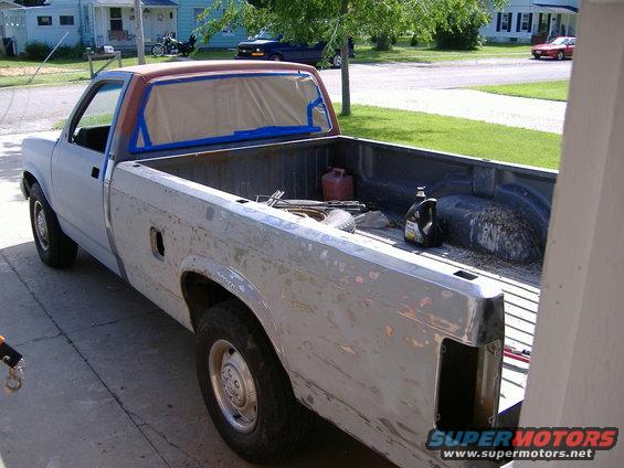 Pickup truck body is stripped and taped off for painting. Tools and fluids are in the bed
