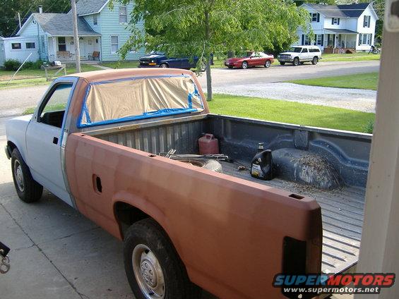 Truck bed with red gas can, oil bottle, and tools. Other vehicles and houses in background
