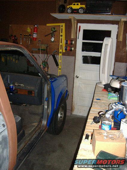 Interior of a blue pickup truck with doors removed, parked in a garage with tools on the wall