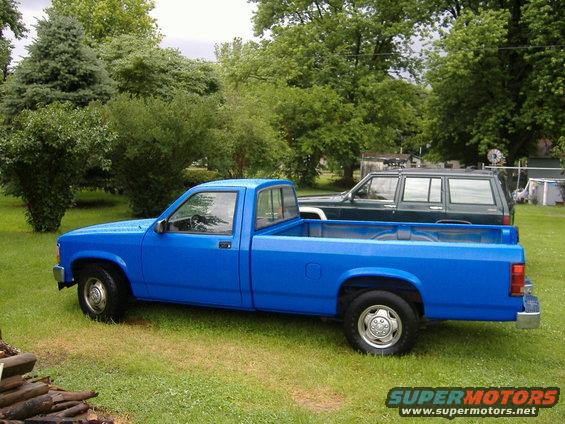 Blue pickup truck parked on grass with a dark SUV behind it