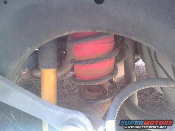 Close-up of red air spring and yellow shock absorber under a vehicle's wheel well