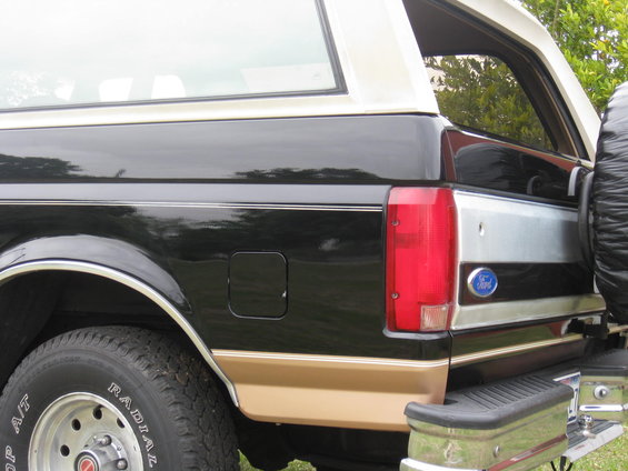 Rear driver's side of a black and tan Ford Bronco, showing the taillight, spare tire mount, and a Ford badge