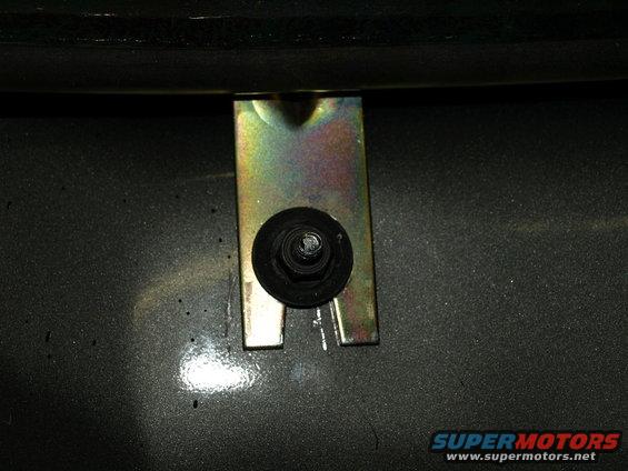 Close-up of a metal bracket and bolt on a dark gray surface. Supermotors.net logo visible