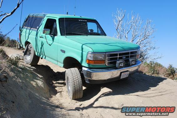 Green 1996 Ford Bronco driving on a dirt trail with a tree in the background