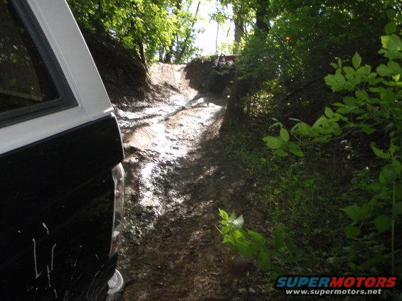 Off-road trail with trees and two vehicles visible in the distance