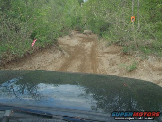 View from inside a vehicle looking at a sandy, rutted off-road track through trees
