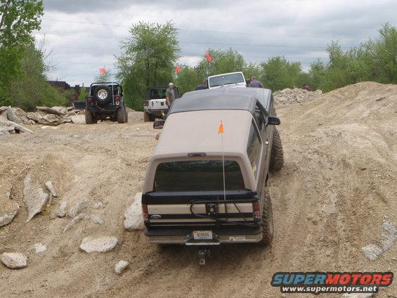 Ford Bronco driving on a dirt trail with other Jeeps behind it