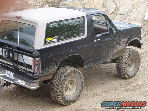 Black Ford Bronco with tan removable top, lifted with off-road tires, covered in mud