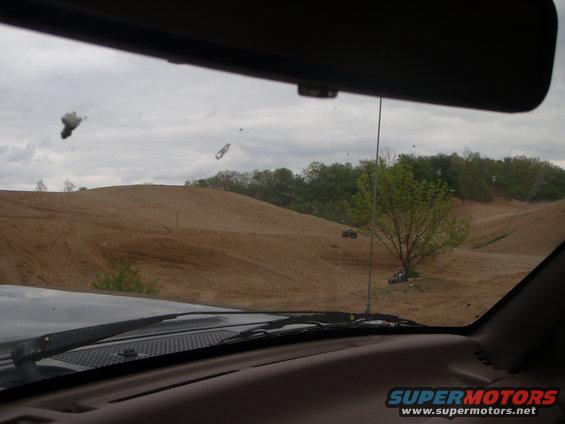 View from inside a vehicle looking out at a sandy off-road park with ATVs on the trails