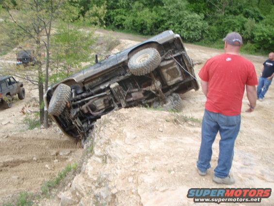 off-road vehicle flipped on its side on a dirt hill with people watching