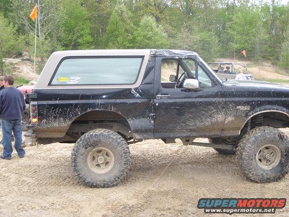 Black 1996 Ford Bronco with a tan top, covered in mud, parked on a dirt track