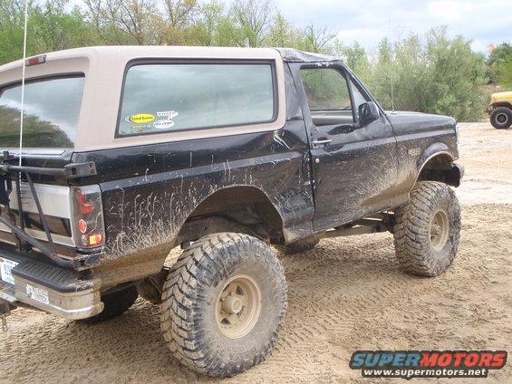 Black 1996 Ford Bronco with tan top and lifted suspension on sandy terrain
