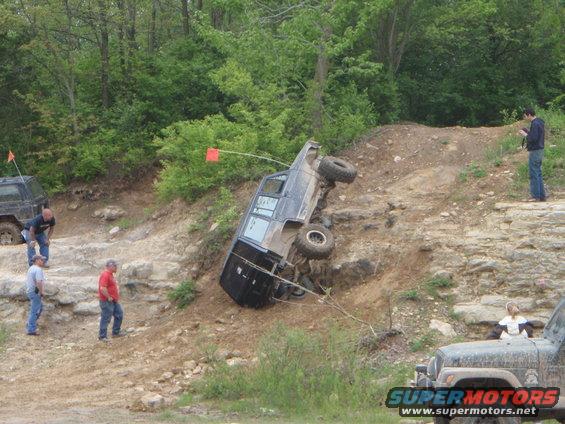 SUV tipped on its side on a dirt hill, people watching