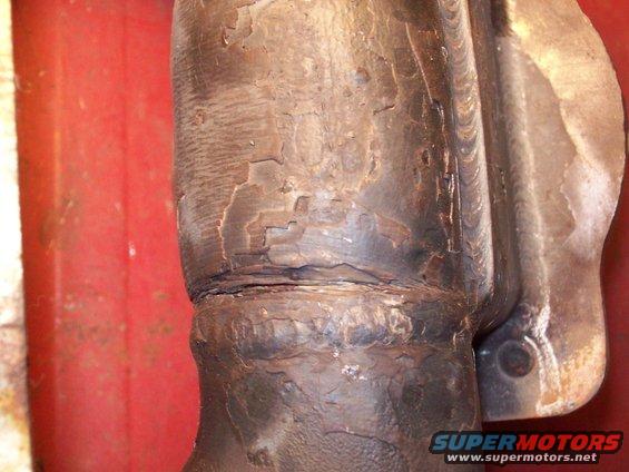 Exhaust manifold with cracked paint and rust, showing weld seams