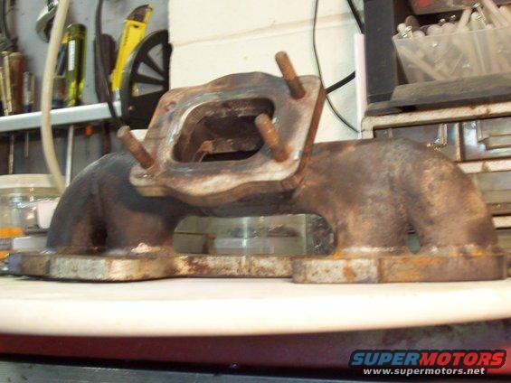 Rusty exhaust manifold with four studs on a workbench