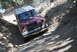 1996 Ford Bronco - A maroon and white Ford Bronco drives on a narrow dirt path with trees and rocks.
