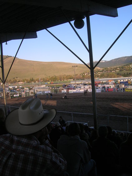 View of a rodeo arena with spectators in the foreground and hills in the background