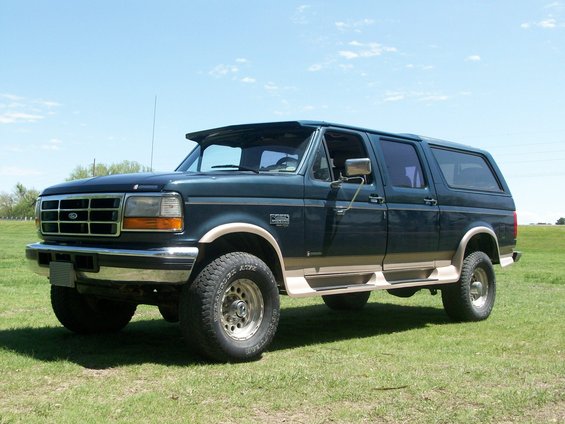 Dark green SUV with tan trim, lifted on off-road tires, parked on grass