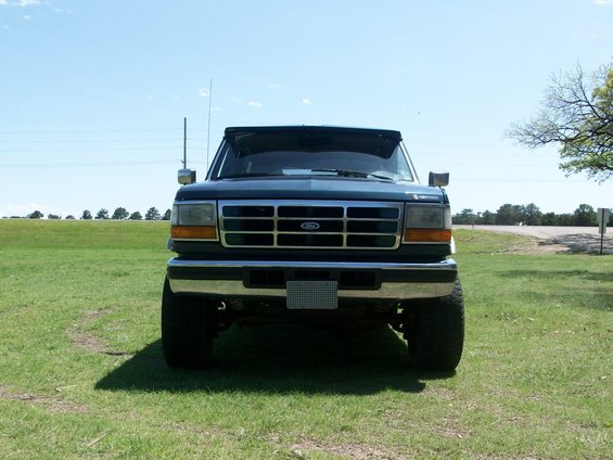 Dark blue Ford truck, front view, parked on grass under a clear sky