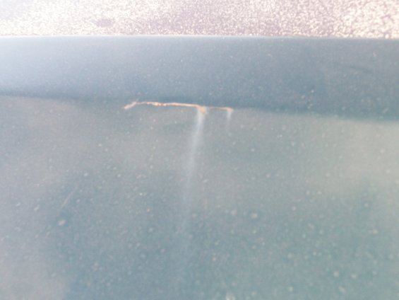 Close-up of a crack in light blue vehicle paint with some rust showing
