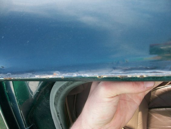 Hand holding open a dark teal car door, showing the edge and interior