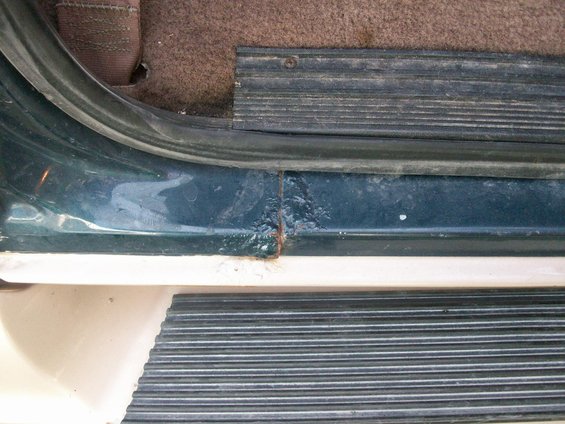 Close-up of a dark green door sill with rust damage and a black ribbed step plate